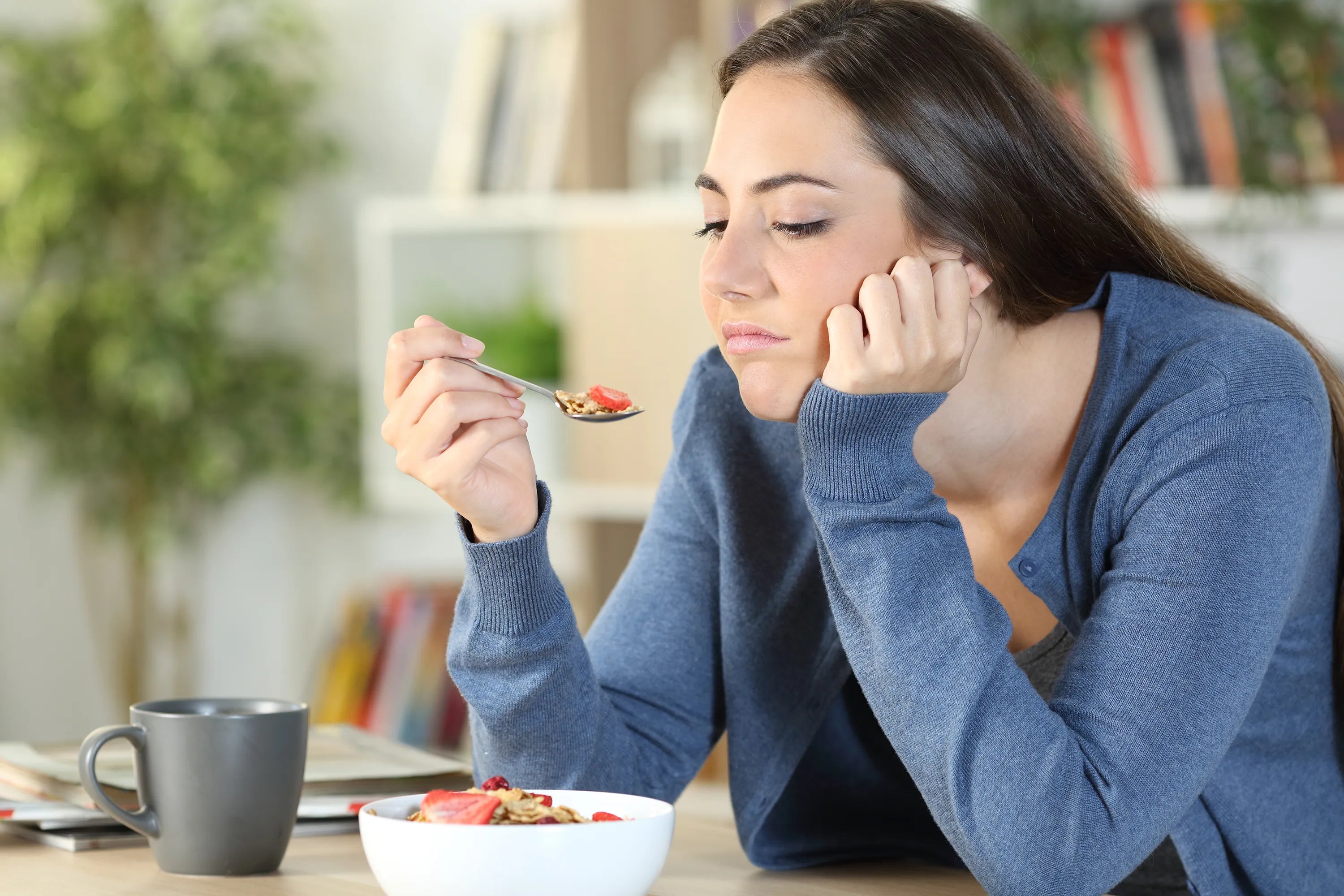 Woman eating a bowl of fruit at a table with a blurred background