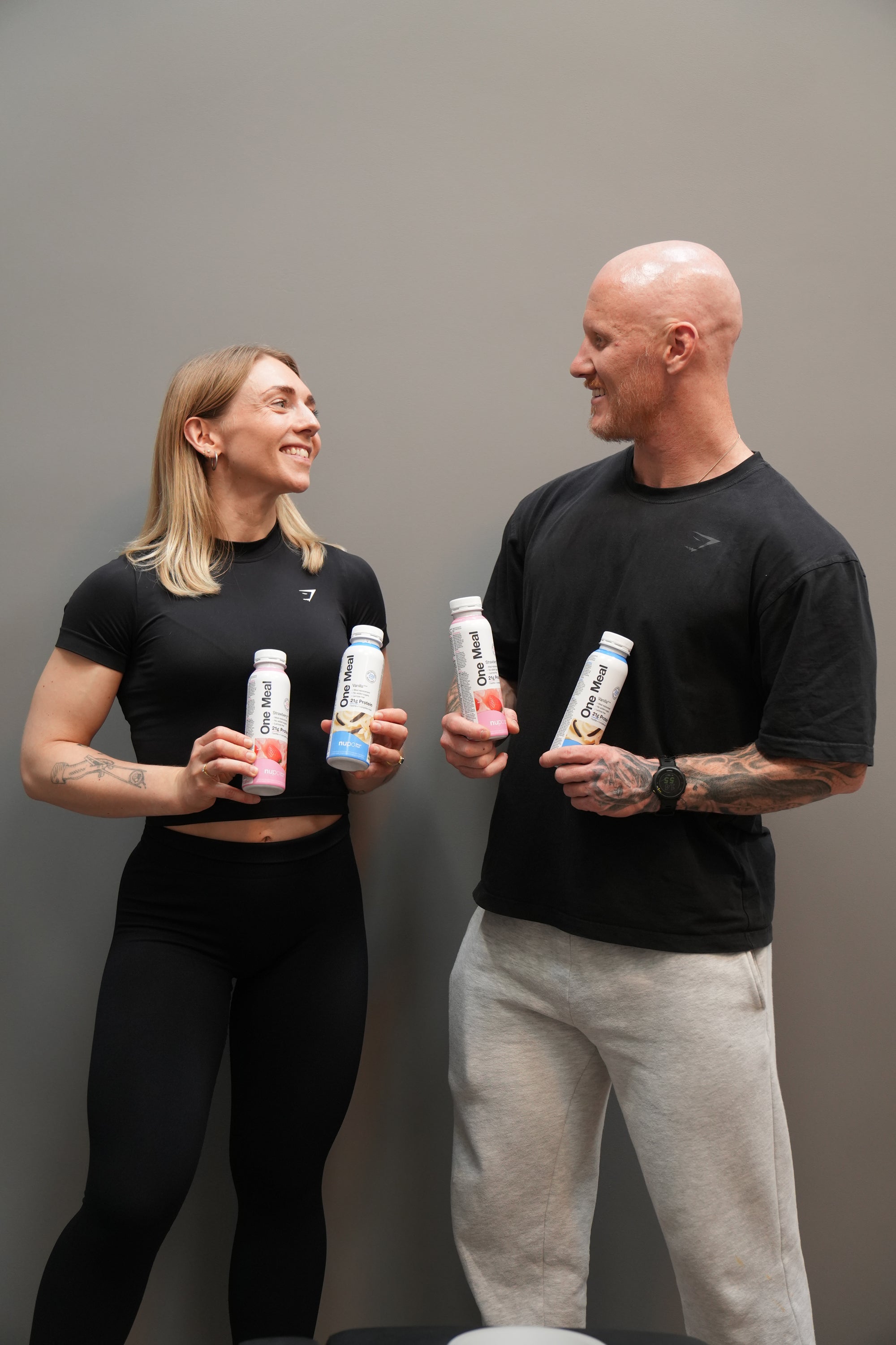 Two people holding bottles against a plain background